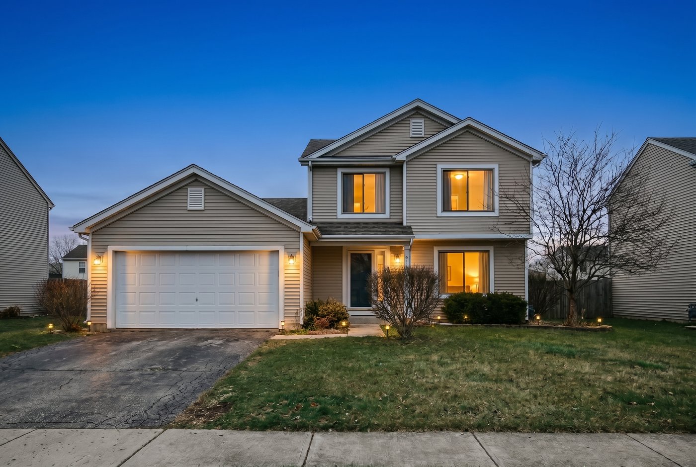 A home exterior at golden-hour twilight with warm glowing windows and a deep blue sky.